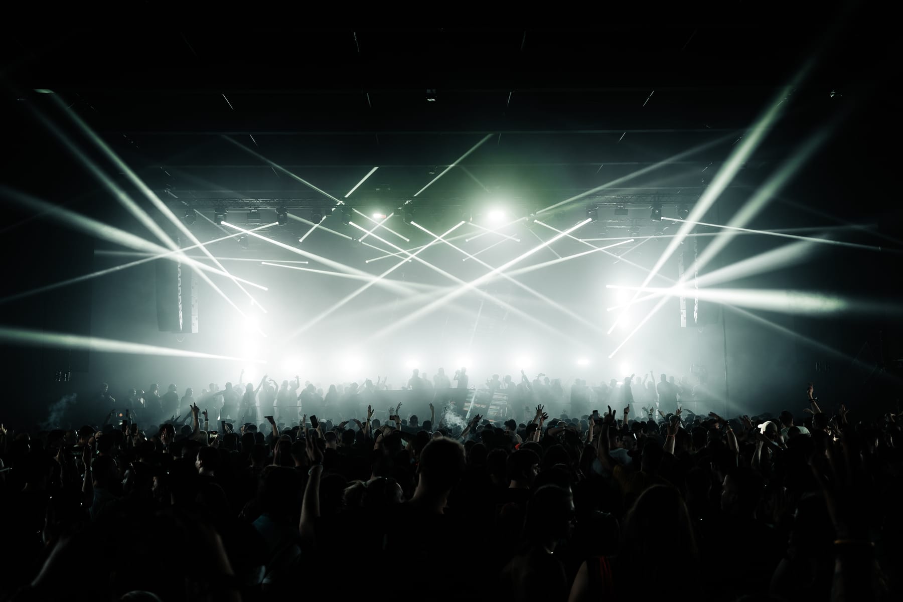 Crossed white light beams cutting through haze above a dark crowd.