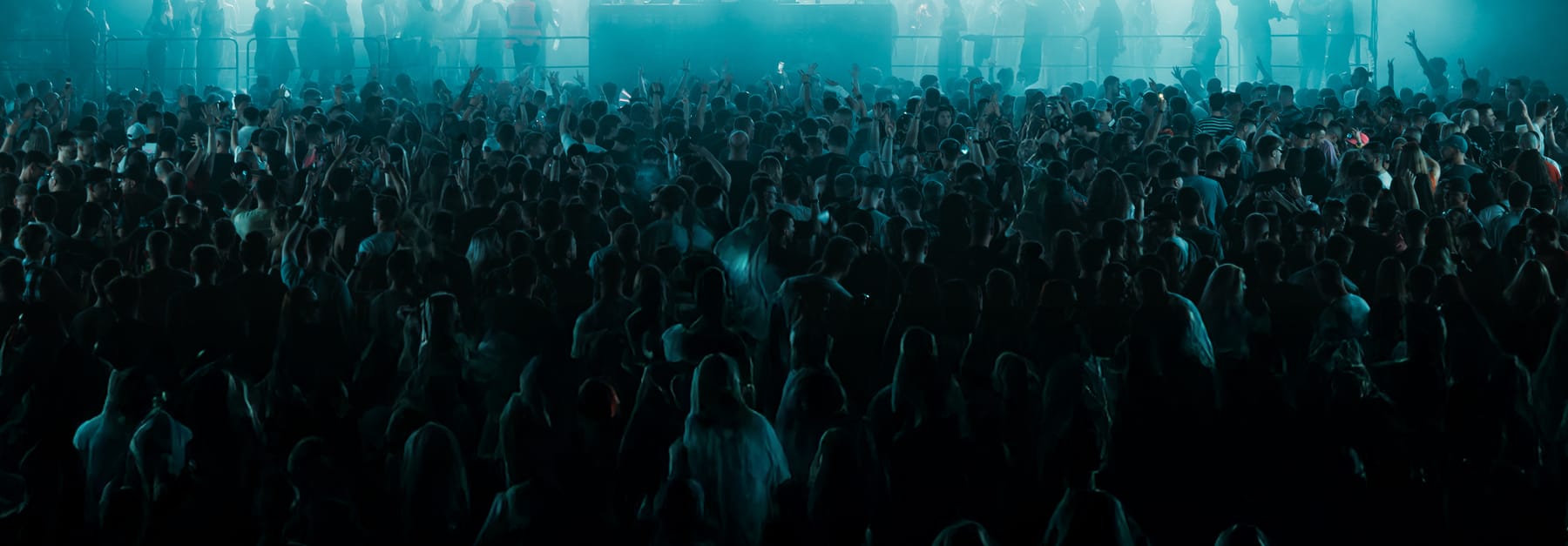 A dense crowd in silhouette under teal stage light.