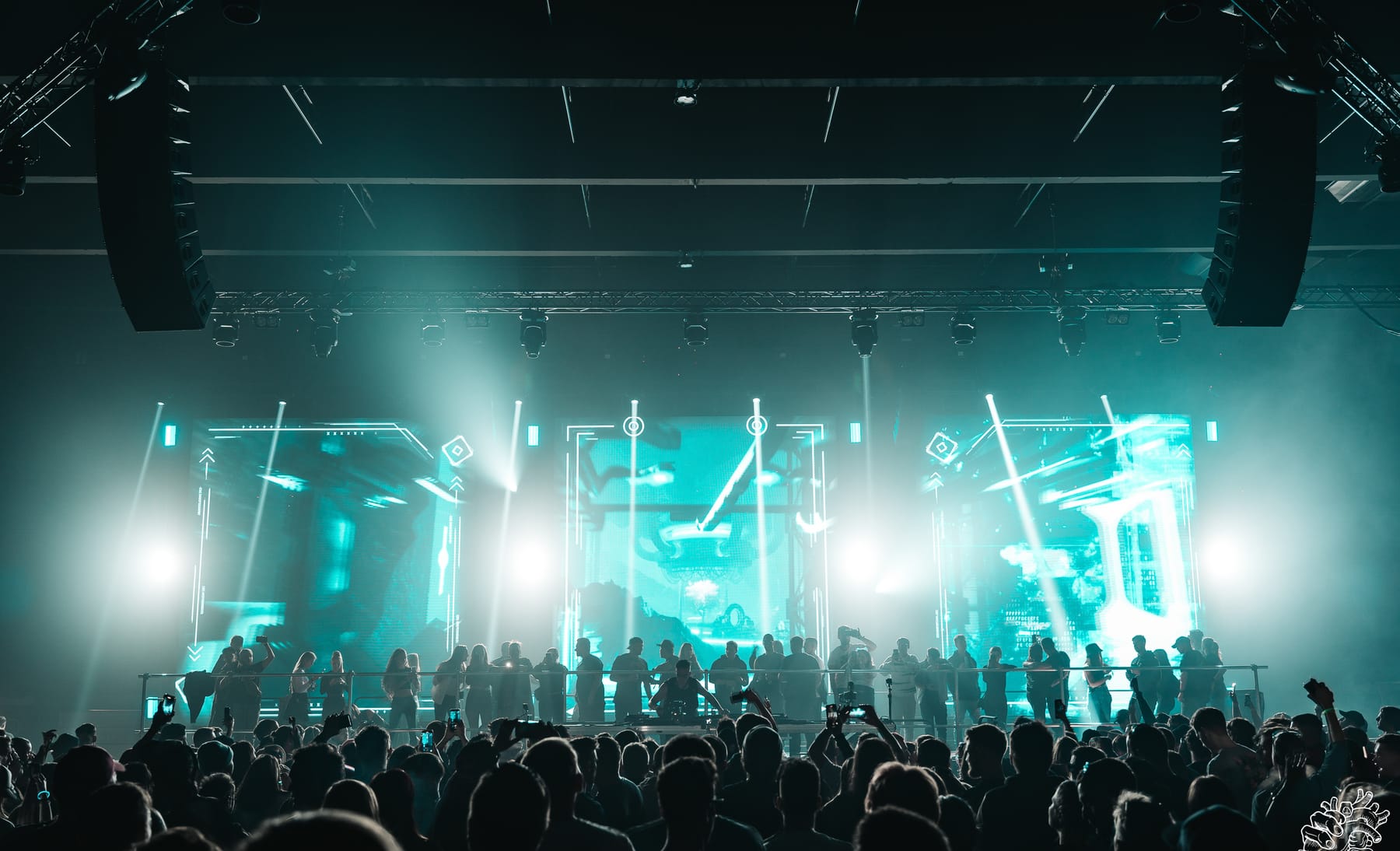 A cyan-lit Pulsation stage with exposed truss, LED panels and beams cutting through haze.